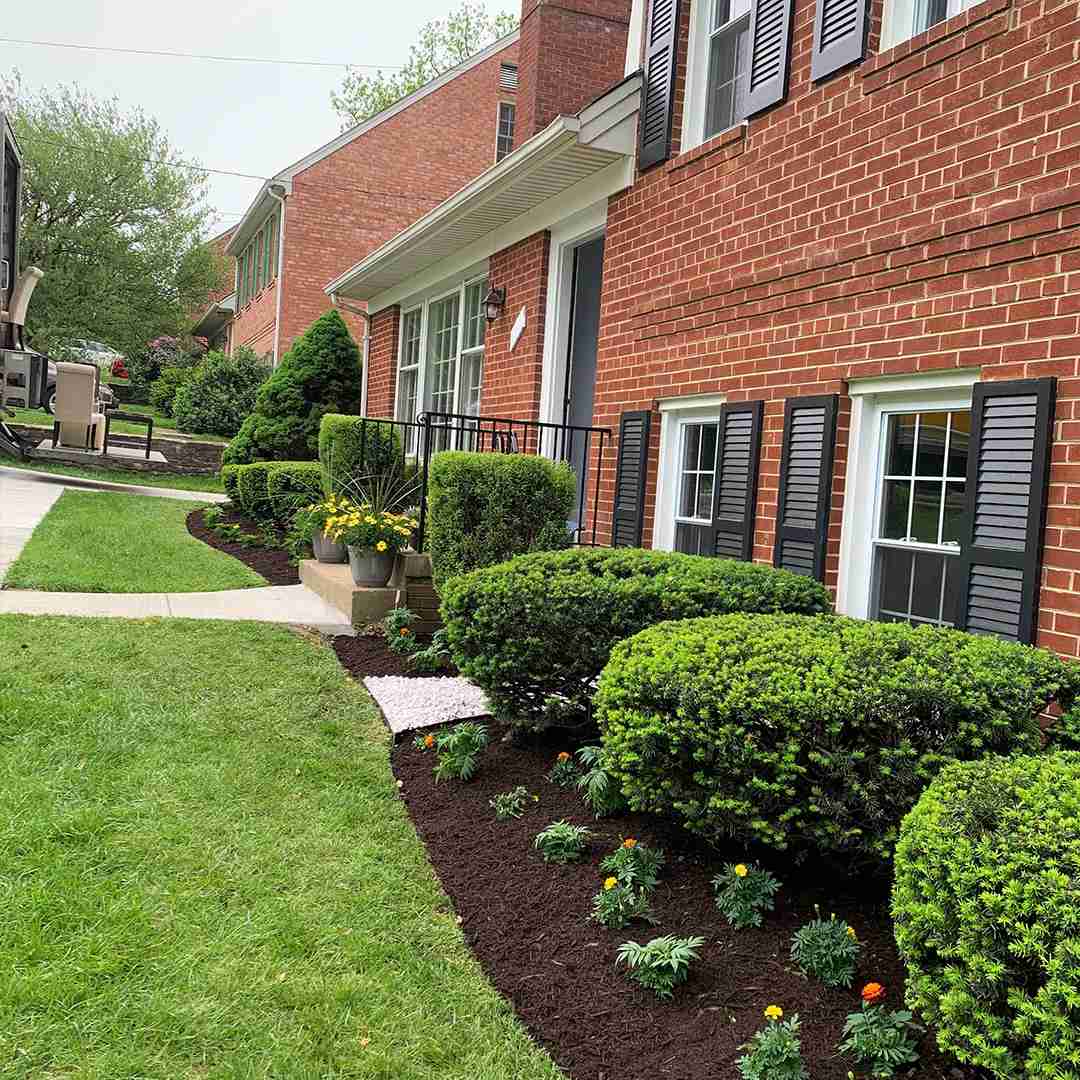 A well-maintained brick house with neatly trimmed bushes and a landscaped garden featuring flowers and fresh mulch.