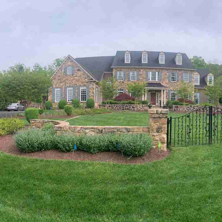 Large stone house with multiple windows, manicured lawn, and an ornate black gate in the foreground.