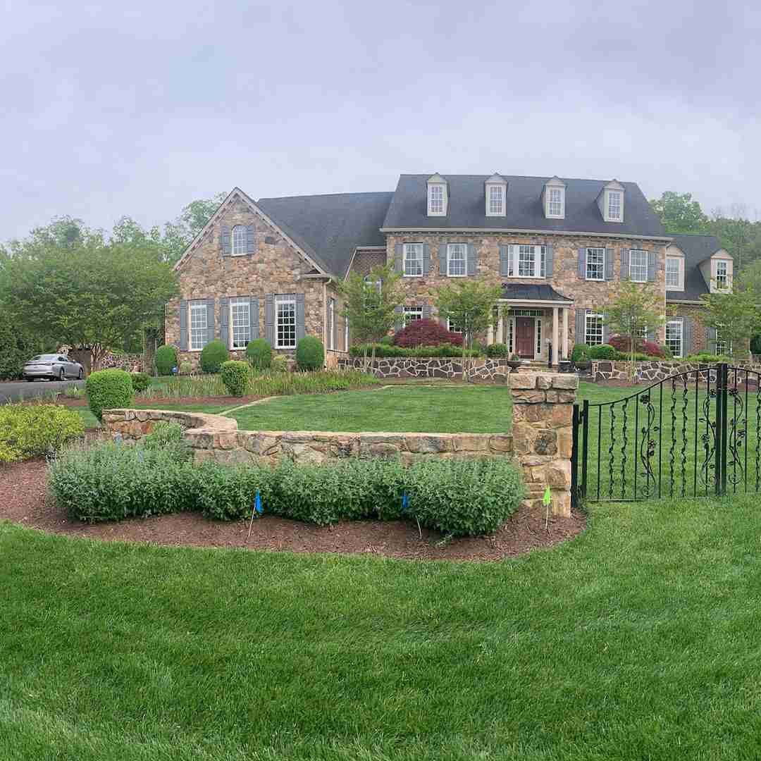 Large stone house with multiple windows, manicured lawn, and an ornate black gate in the foreground.