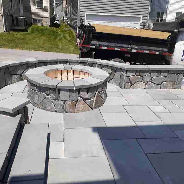 Stone fire pit and surrounding patio area under construction in a residential backyard.