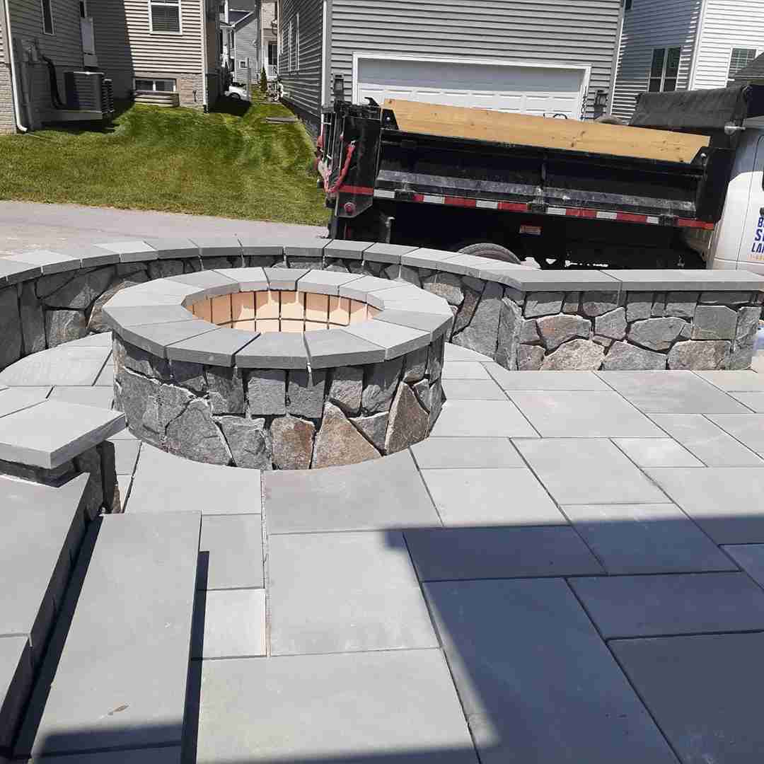 Stone fire pit and surrounding patio area under construction in a residential backyard.