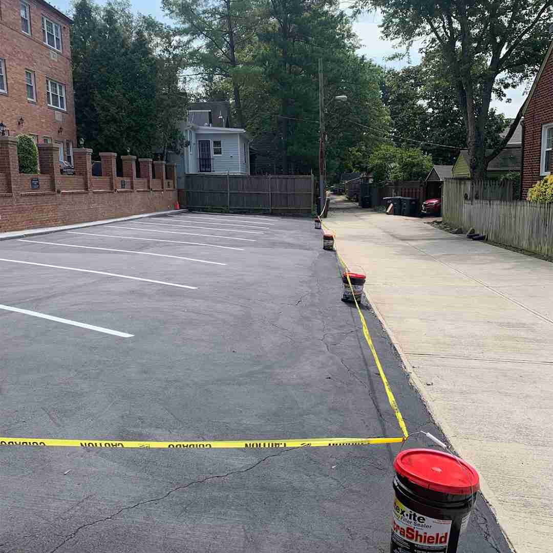 An empty, freshly sealed parking lot with caution tape and buckets along the perimeter.