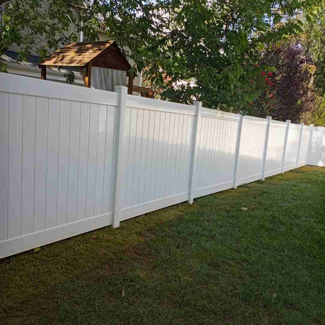 White vinyl privacy fence bordering a backyard with green grass and a small wooden playhouse in the background.