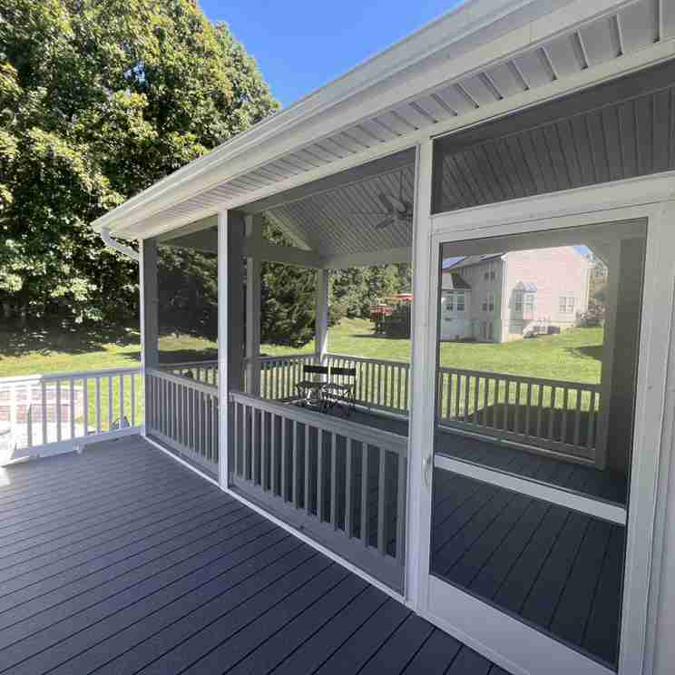 Screened porch with white railings and a small patio set, adjacent to a grassy yard with trees and a neighboring house.