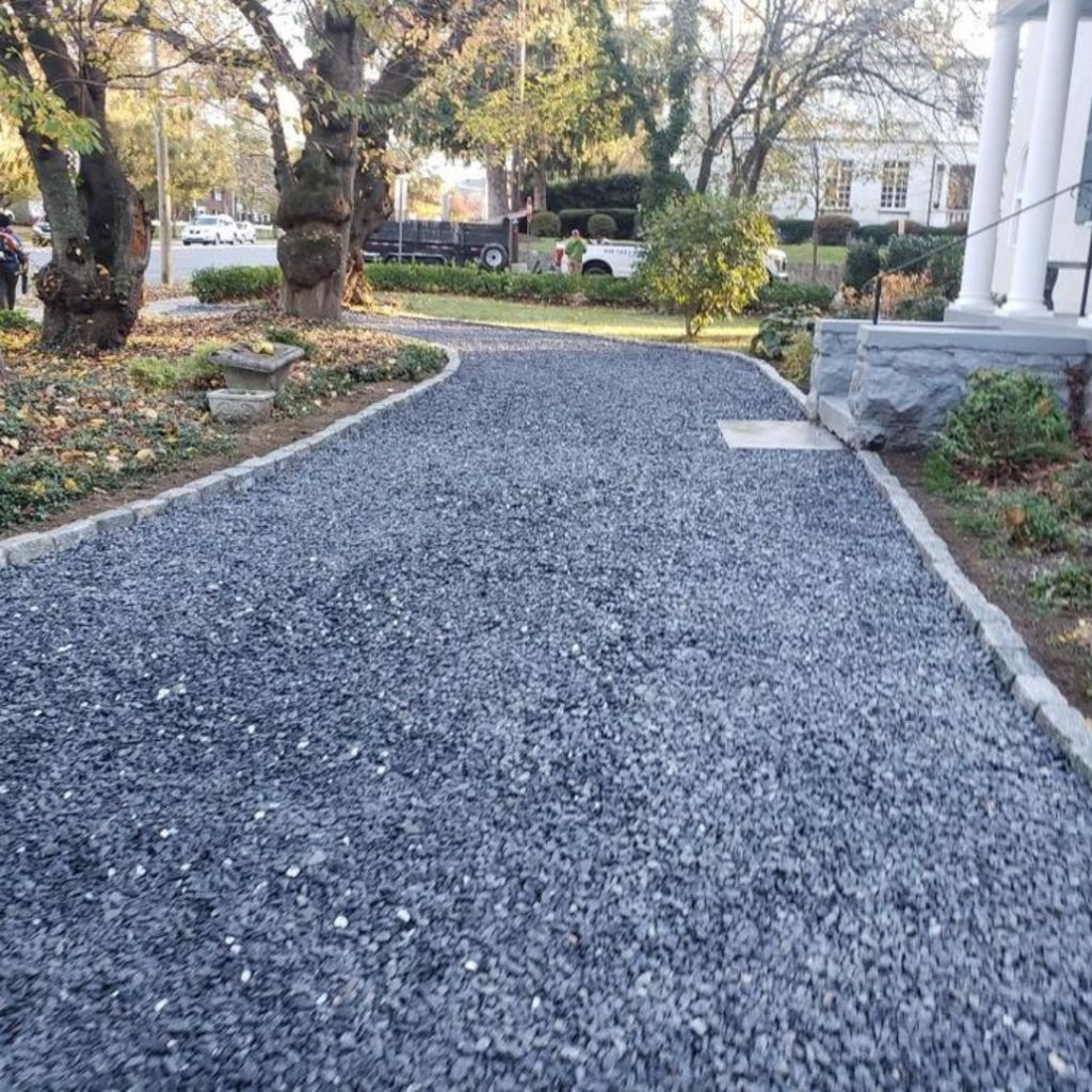 Gravel path leading to a white building surrounded by trees and greenery.