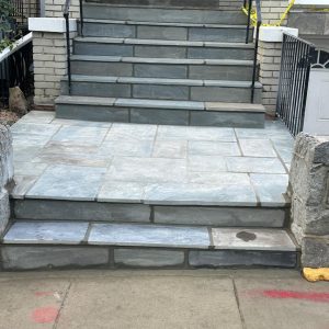 Stone steps leading up to a brick building with a metal railing and caution tape.