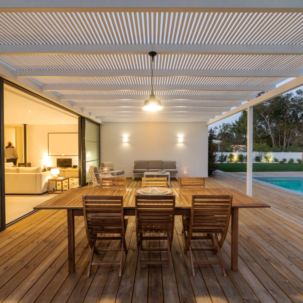 Outdoor dining area with wooden table and chairs under a pergola at night.