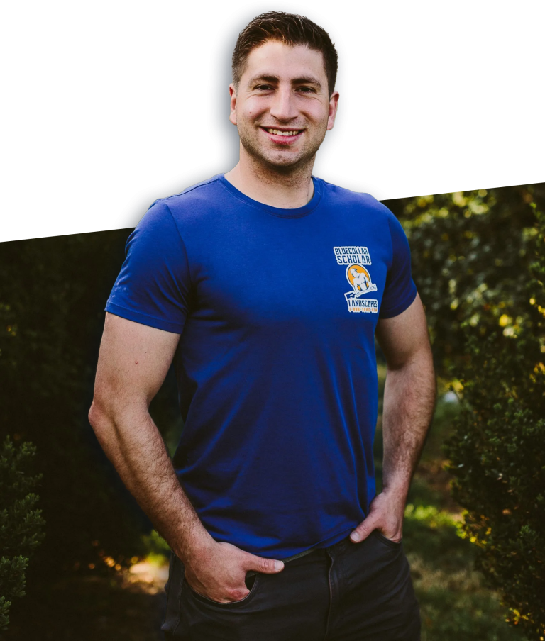 A man in a blue t-shirt with "Blue Collar Scholar Landscapes" logo stands smiling with hands in pockets, outdoors with greenery in the background.