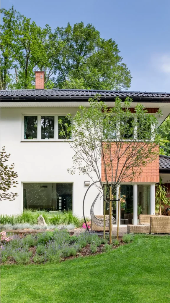 Modern house with white and brick exterior, surrounded by lush greenery and a well-kept lawn.