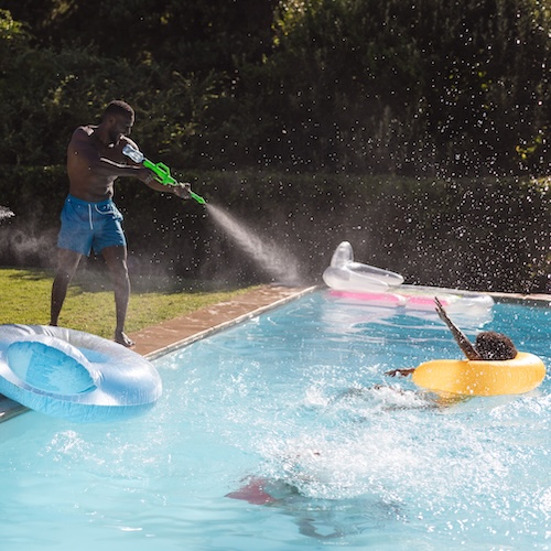 Person spraying water with a toy gun at people in a pool, causing splashes.