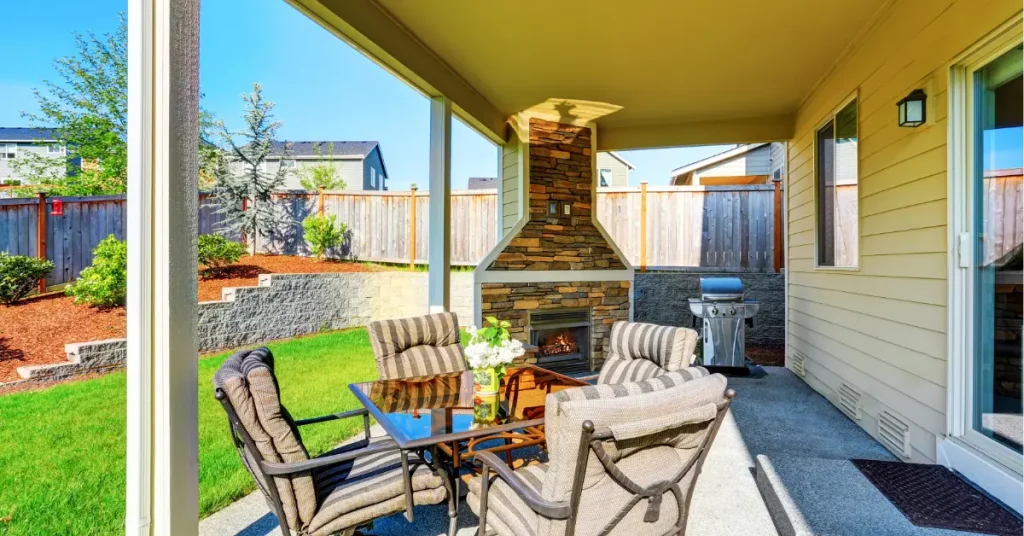 Bright covered patio with outdoor fireplace and seating area in residential backyard with green lawn