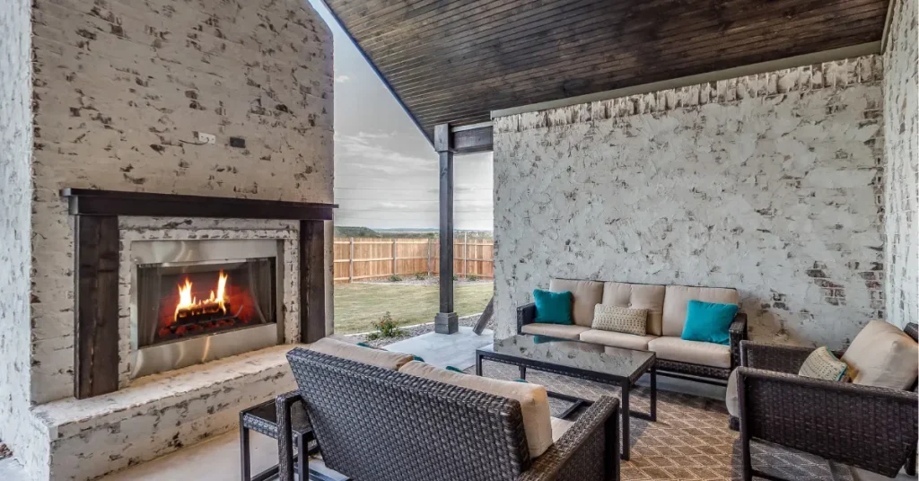 Elegant covered outdoor patio featuring built-in stone fireplace with comfortable seating area and modern design