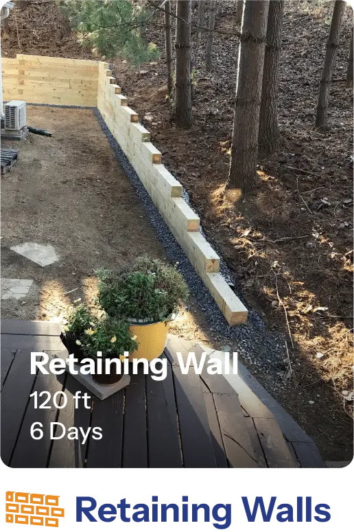 Image of a 120-foot retaining wall built in six days, showcasing a wooden structure along a landscaped area bordered by trees. A potted plant is visible in the foreground, highlighting the outdoor setting.