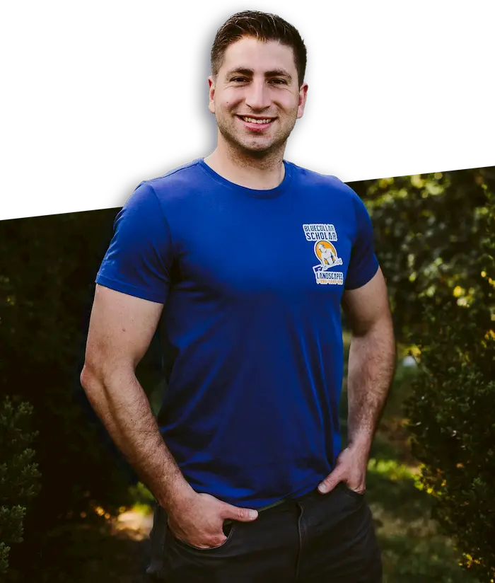 Person wearing blue t-shirt with a logo, standing outdoors with hands in pockets.