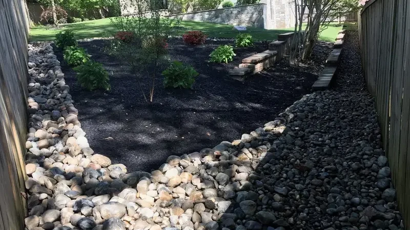 River gravel swale running between two fences in a backyard, designed to slow and direct stormwater toward a safe outlet.