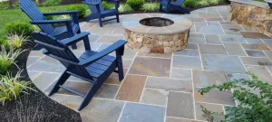 What is Flagstone? Here is a patio with blue chairs and a stone fire pit on a multicolored flagstone surface.