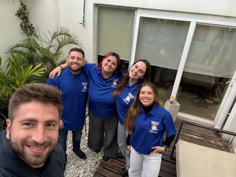 Five people smiling in a courtyard, with four wearing matching blue shirts.