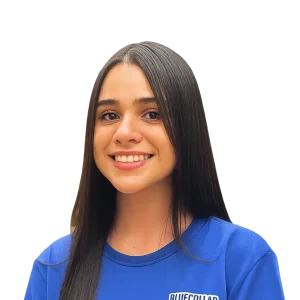 Smiling person with long hair wearing a blue shirt on a plain background.