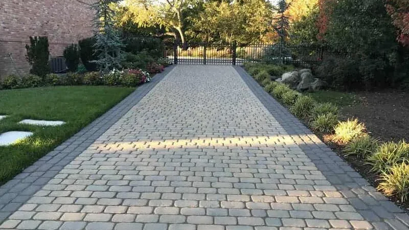 Cobblestone driveway lined with grass and plants, leading to a metal gate.