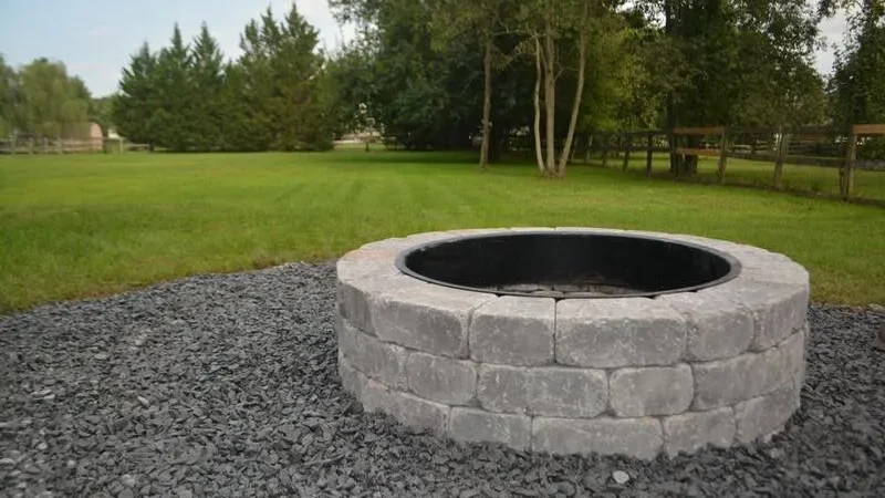 Stone fire pit surrounded by gravel in a grassy backyard.