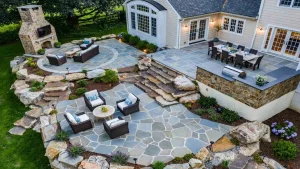 Flagstone patio with outdoor seating, a dining table, and a fireplace, surrounded by landscaped plants and rocks.