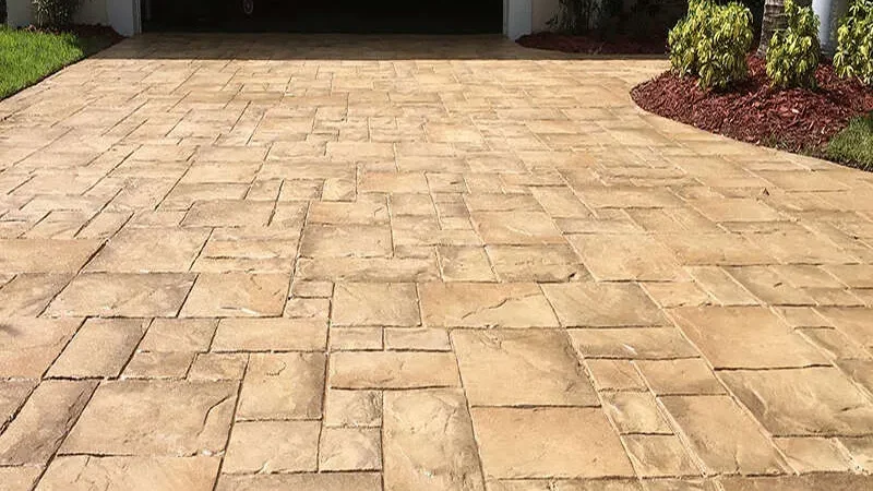 A stamped concrete driveway leading to a garage, surrounded by plants and mulch.