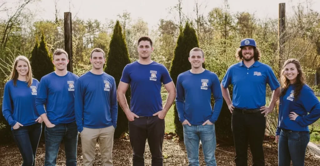 Seven people in matching blue shirts pose outdoors in front of trees.