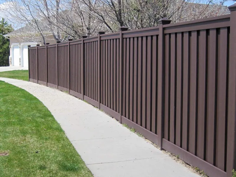 Types of Fences: A long brown composite fence lines a curved sidewalk with grass on one side.