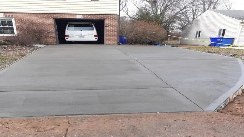 Newly paved concrete driveway leading to a garage with a white vehicle inside.