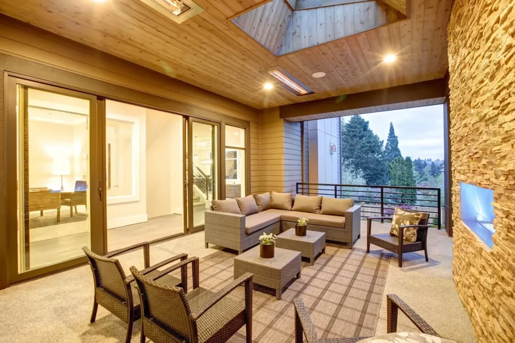 Cozy covered patio with wicker furniture, a stone fireplace, and a view of trees.