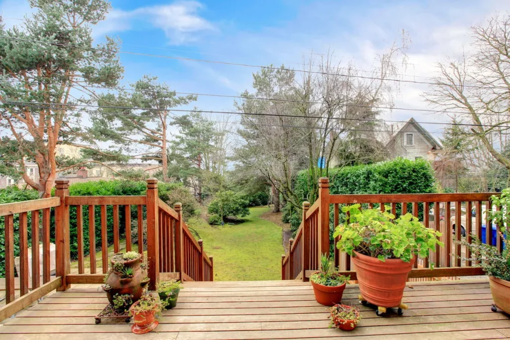 Wooden deck with potted plants overlooking a grassy backyard and trees.