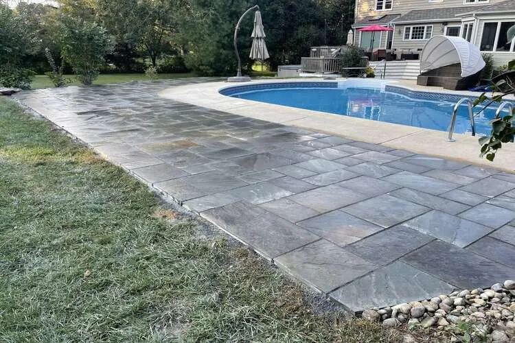 Backyard with a paved patio and a curved swimming pool beside a house.