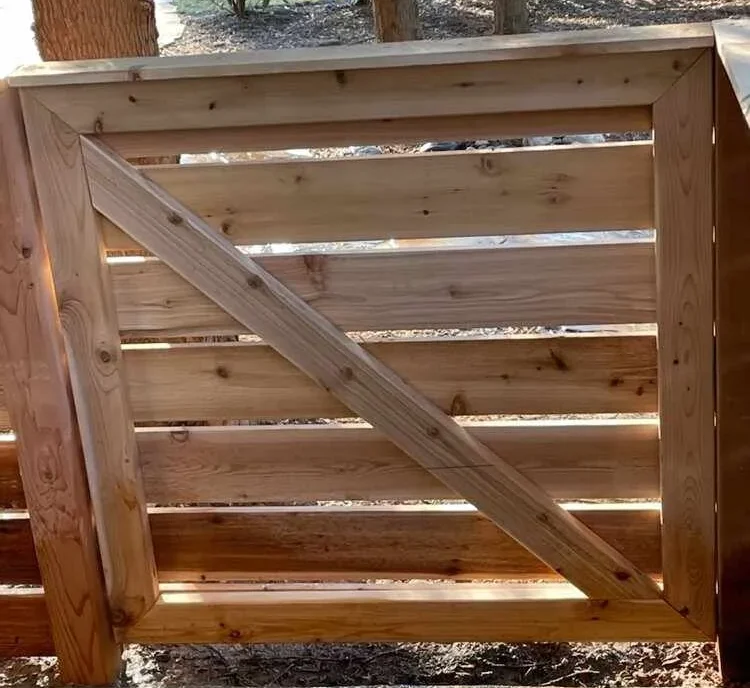 Wooden gate with horizontal planks and a diagonal support, set in a garden area.