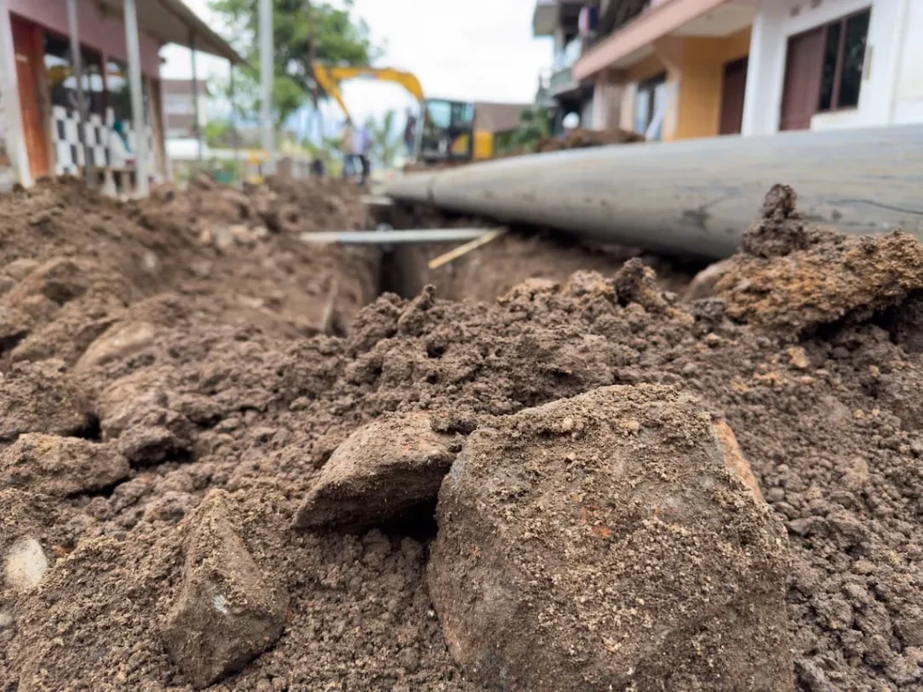 Close-up of a construction site with exposed dirt and a large pipe being installed.