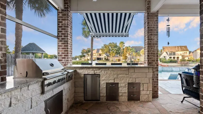 Outdoor kitchen with a grill and a view of a pool and houses in the background.
