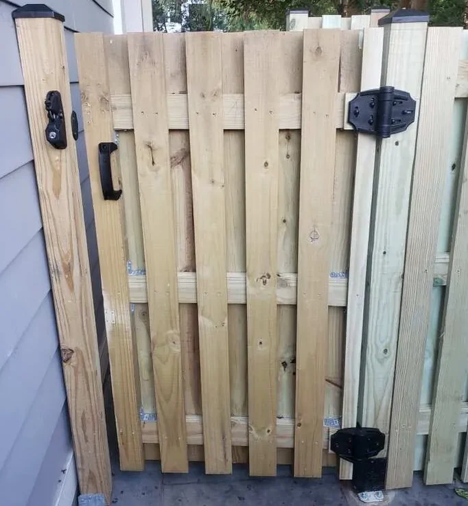 Wooden gate with metal hinges and latch, positioned next to a house wall.