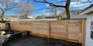 Gate Ideas: Wooden backyard fence with a stone patio and leafless trees under a blue sky.