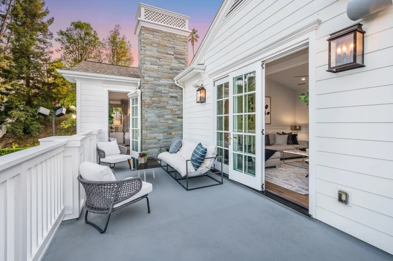 Cozy outdoor patio with cushioned seating, adjacent to an open living room, against a sunset backdrop.
