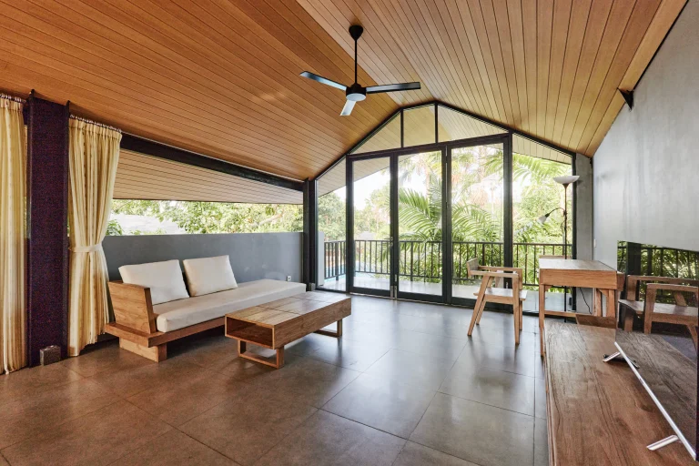 Spacious room with wooden furniture, large windows, and a view of lush greenery.