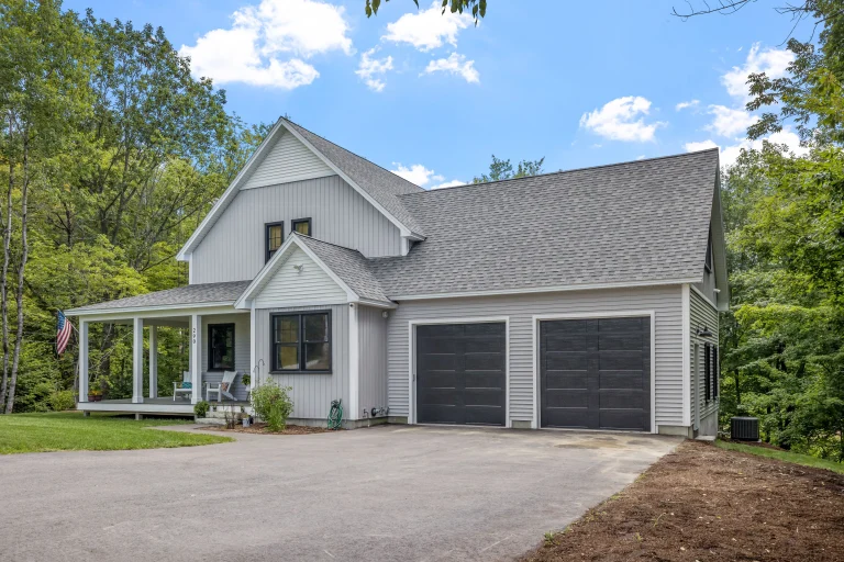 Gray house with porch, American flag, and two-car garage surrounded by trees, built by home addition contractors.