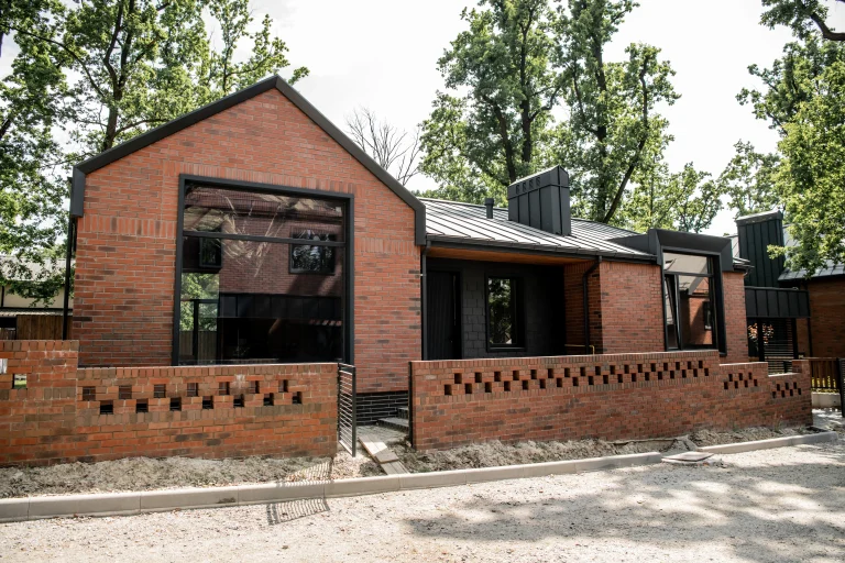A modern brick house with large windows and a decorative brick fence, surrounded by trees.