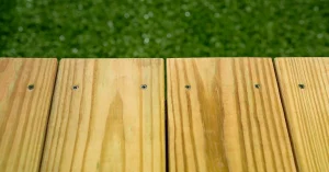 Wooden deck planks with screws, against a blurred green grass background.