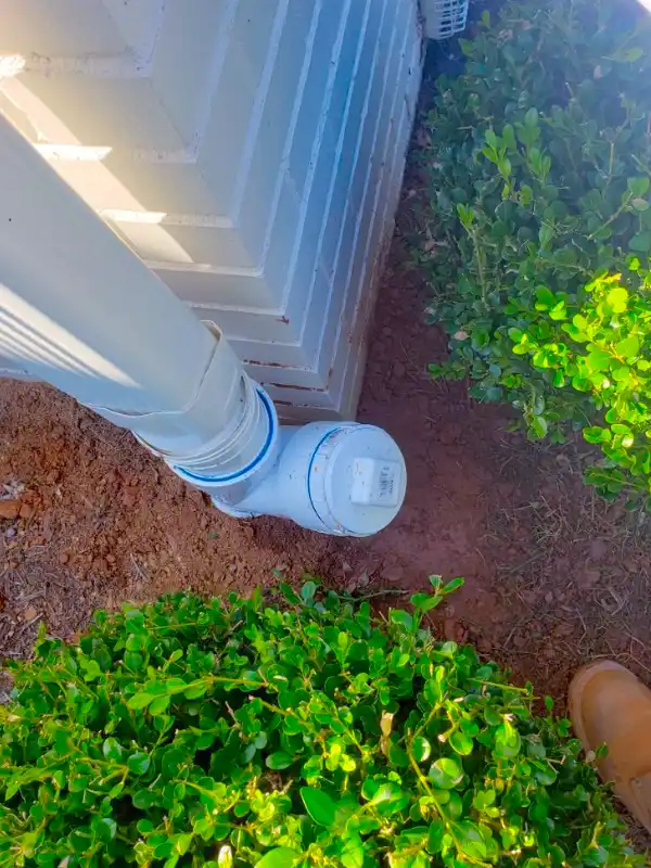 A professional downspout extension installation in the DMV area featuring a white PVC transition and a threaded cleanout adapter.