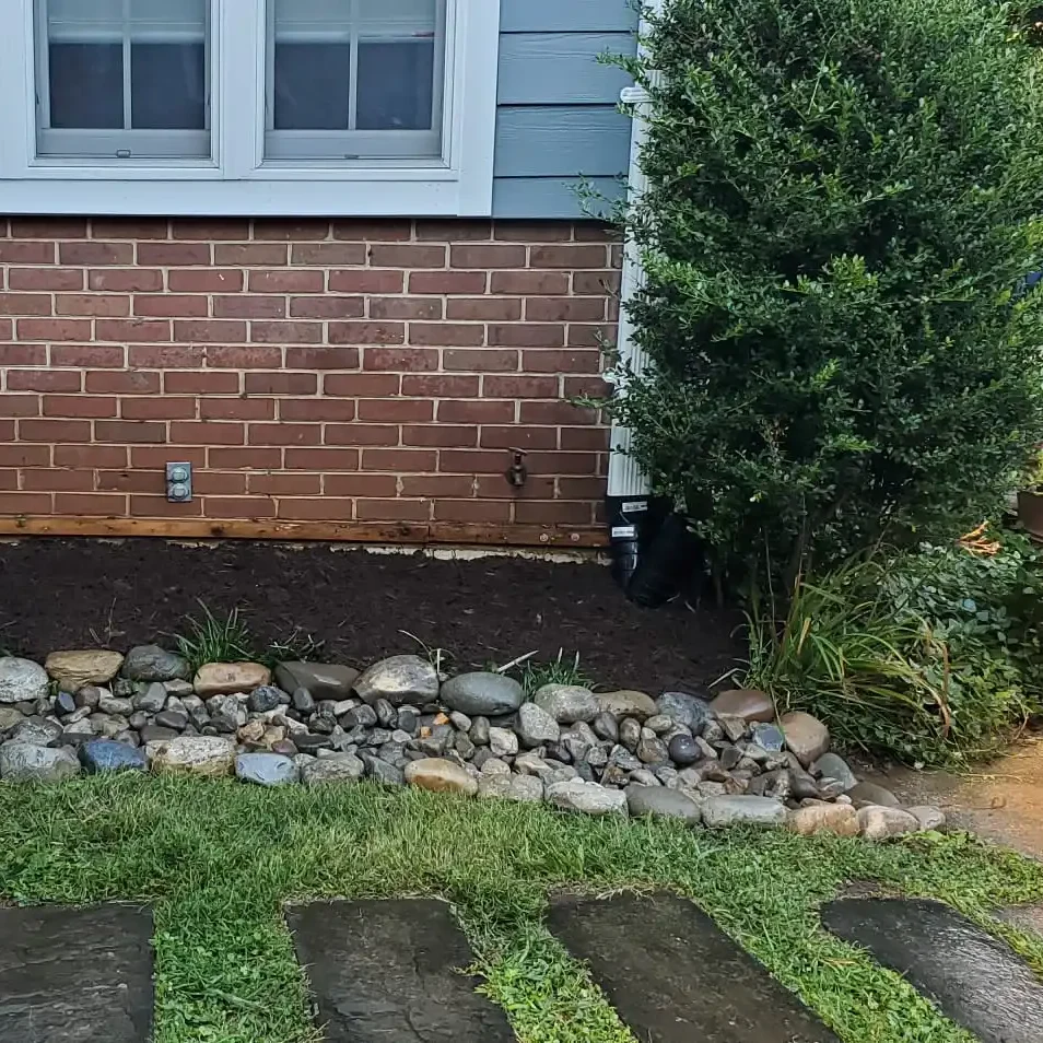 A functional and decorative dry creek bed made of river stones installed alongside a fresh mulch bed for improved home drainage.