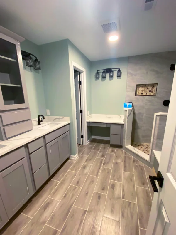 Modern Maryland bathroom remodel featuring grey shaker cabinets, white quartz countertops, a custom walk-in tile shower, and wood-look plank flooring.