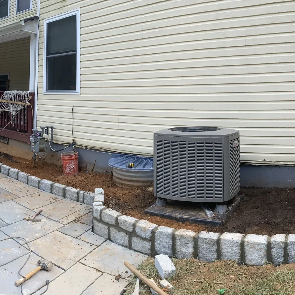 Ongoing backyard renovation showing a large slate-grey paver patio and a raised Belgian block cobblestone border surrounding HVAC units.