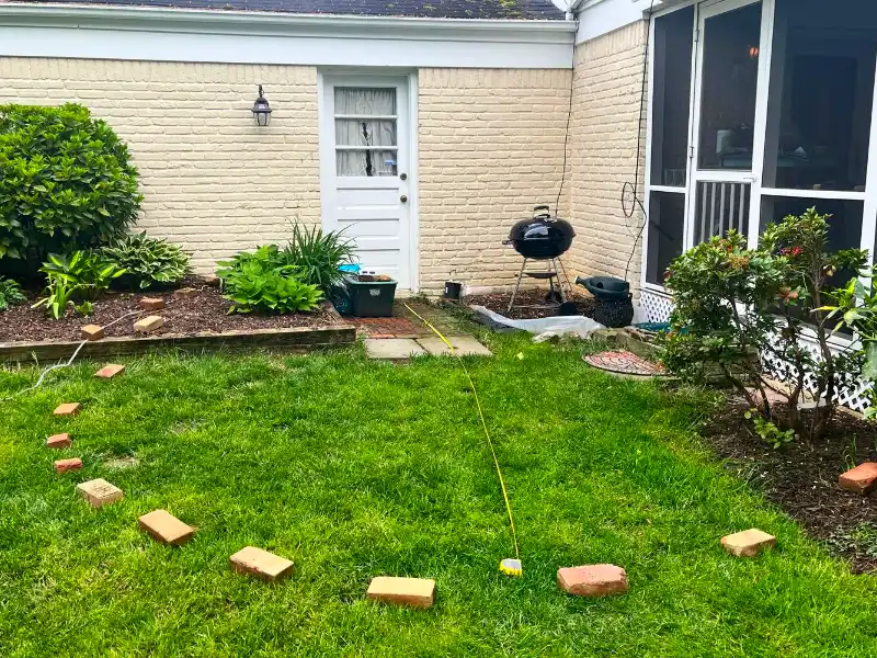 Backyard patio area marked with curved brick layout before excavation and flagstone patio installation