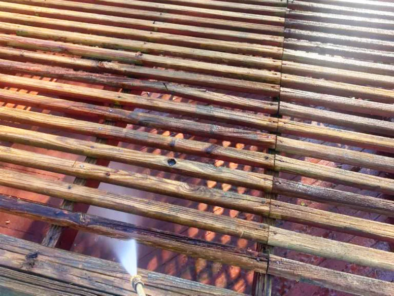 Wooden parts of a deck and pergola being pressure-washed as part of the finishing process