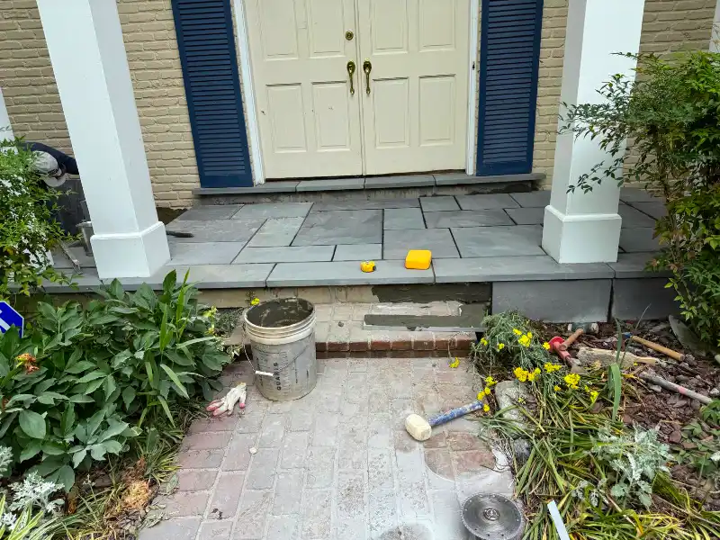 Front porch with newly installed gray flagstone near white double doors and tools during stone veneer installation