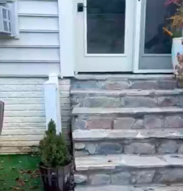 Before photo of exterior stone steps with an old vinyl railing positioned away from the stair edge.